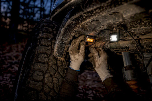Hands installing amber and white rock lights under vehicle